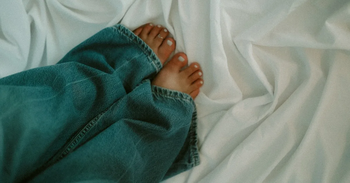 Jambes au repos sur des draps blancs illustrant le syndrome des jambes sans repos